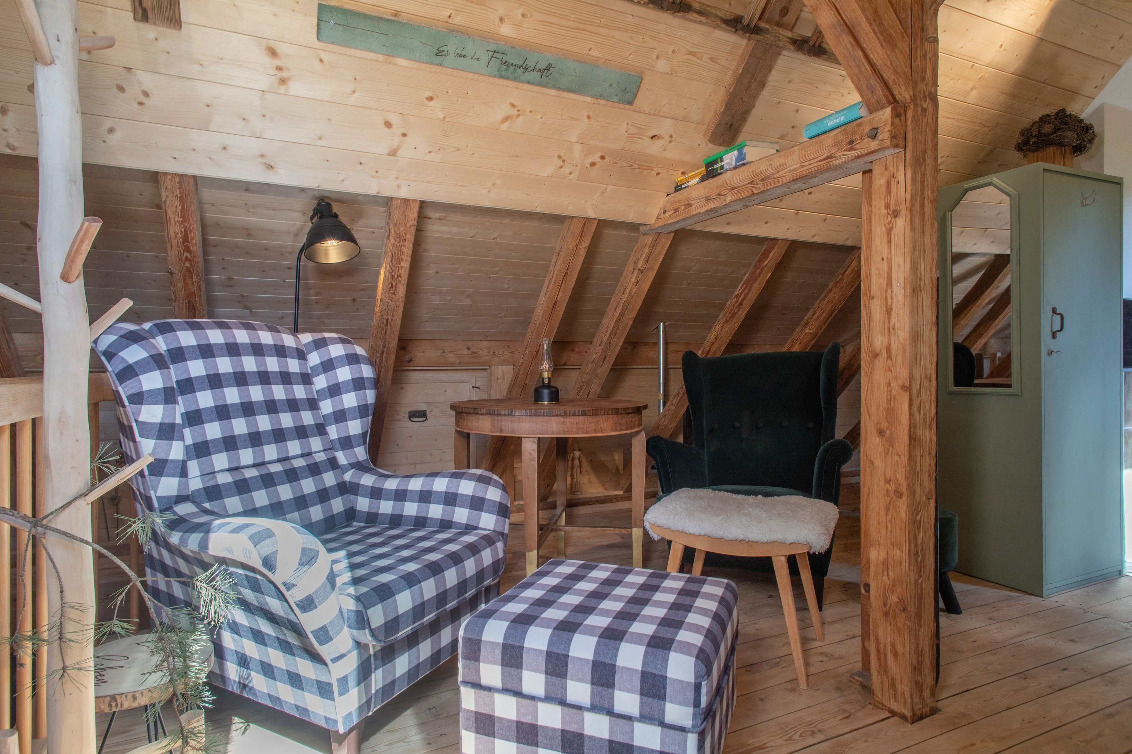 Ein gemütliches Dachzimmer mit einem karierten Sofa, einem Sessel, einem kleinen Tisch und einer Lampe.