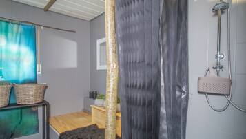 Ein Badezimmer mit Dusche, Holzboden, einem kleinen Tisch mit Körben und einem Fenster mit Vorhang.