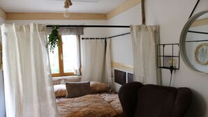 Una habitación con una cama cubierta de paja, un sillón de cuero marrón y una ventana con una planta colgando en el exterior.