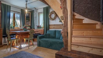 Uma sala de estar aconchegante com escada de madeira, área de jantar com mesa e cadeiras, e sofá verde.