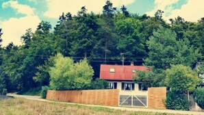 Una casa con techo rojo, rodeada de un bosque denso y una valla de madera.