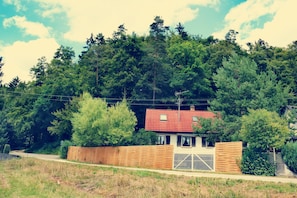Una casa con techo rojo, rodeada de un bosque denso y una valla de madera.