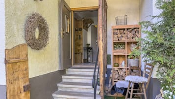 Eine Holztür mit einem Schild, eine Treppe, die zu einem Raum führt, ein Holzregal mit Holzscheiten und eine Pflanze.