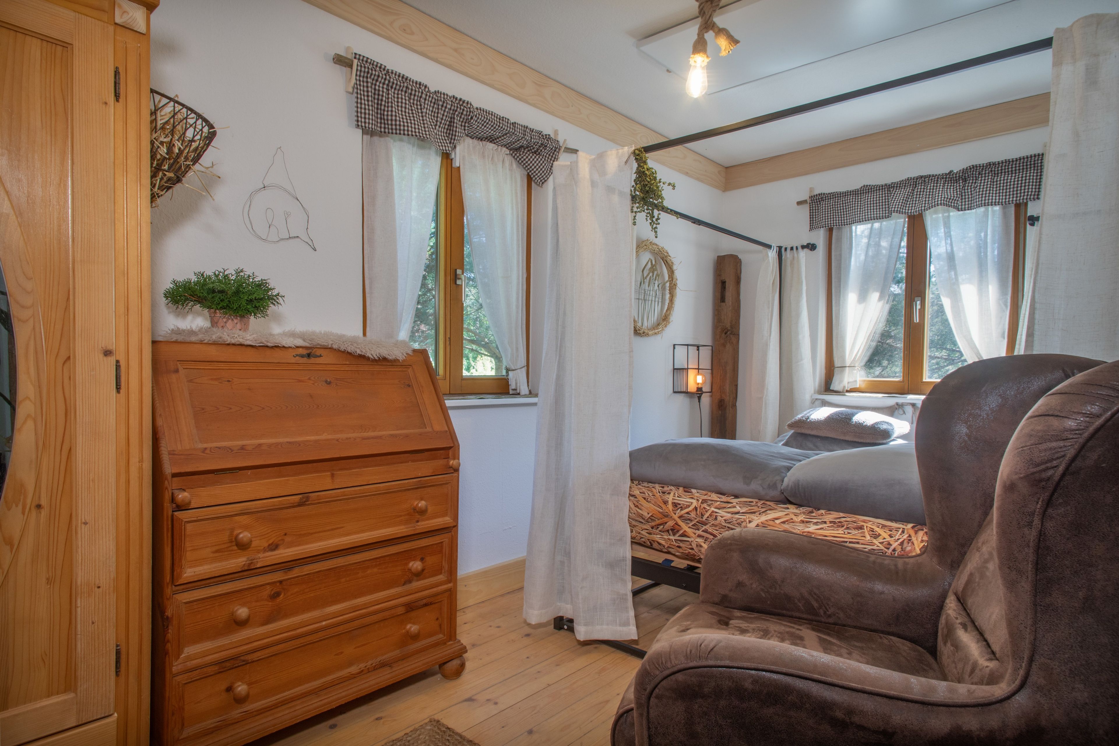 A cozy room with a wooden dresser, a plush armchair, and a bed with a straw mattress.