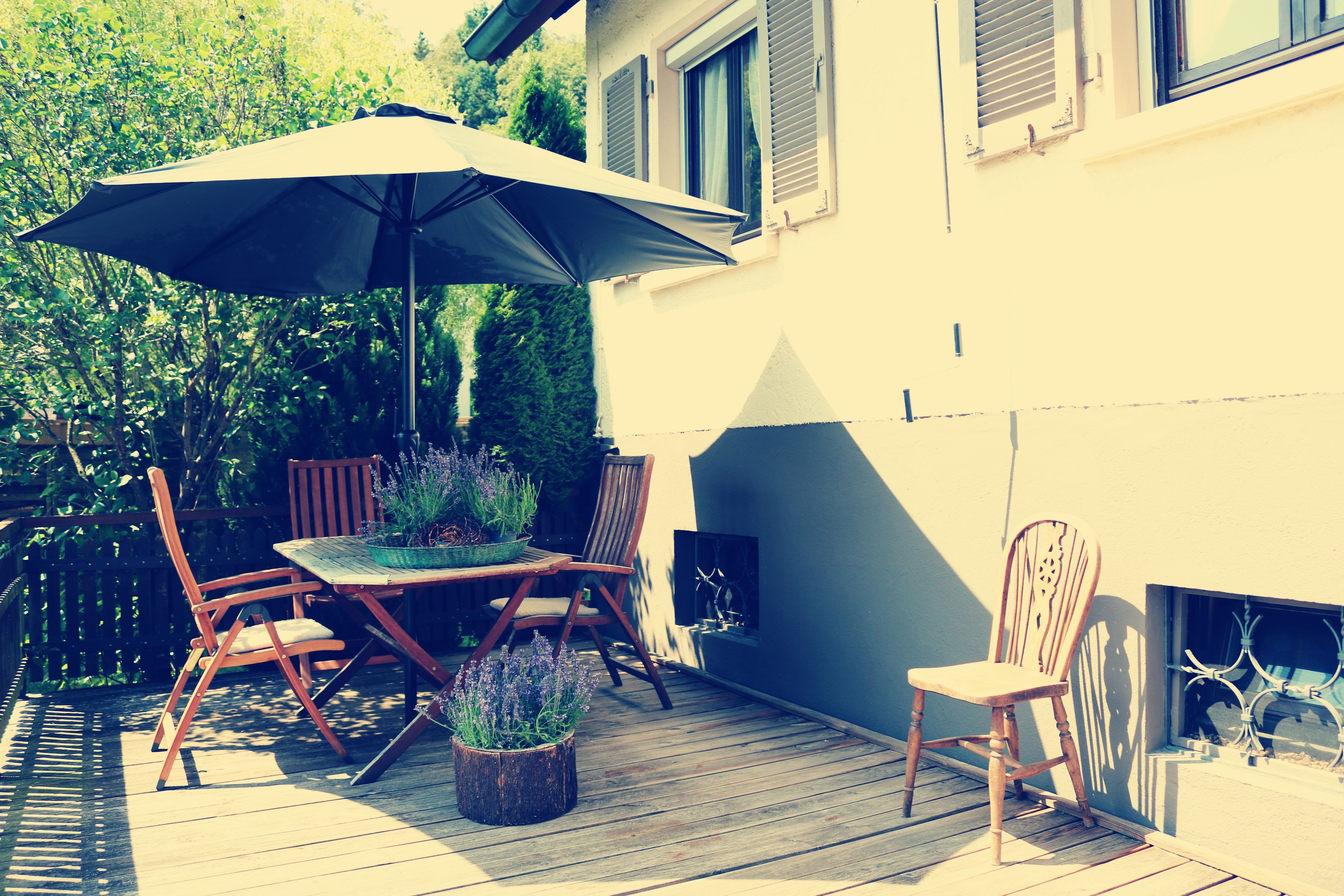 Eine Terrasse im Freien mit Tisch, Stühlen, Sonnenschirm und Blumentöpfen.