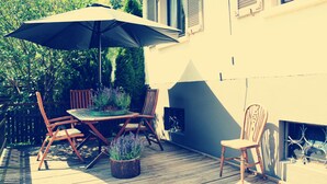 Un patio al aire libre con mesa, sillas, una sombrilla y plantas en macetas.