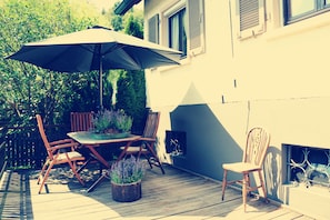Un patio al aire libre con mesa, sillas, una sombrilla y plantas en macetas.