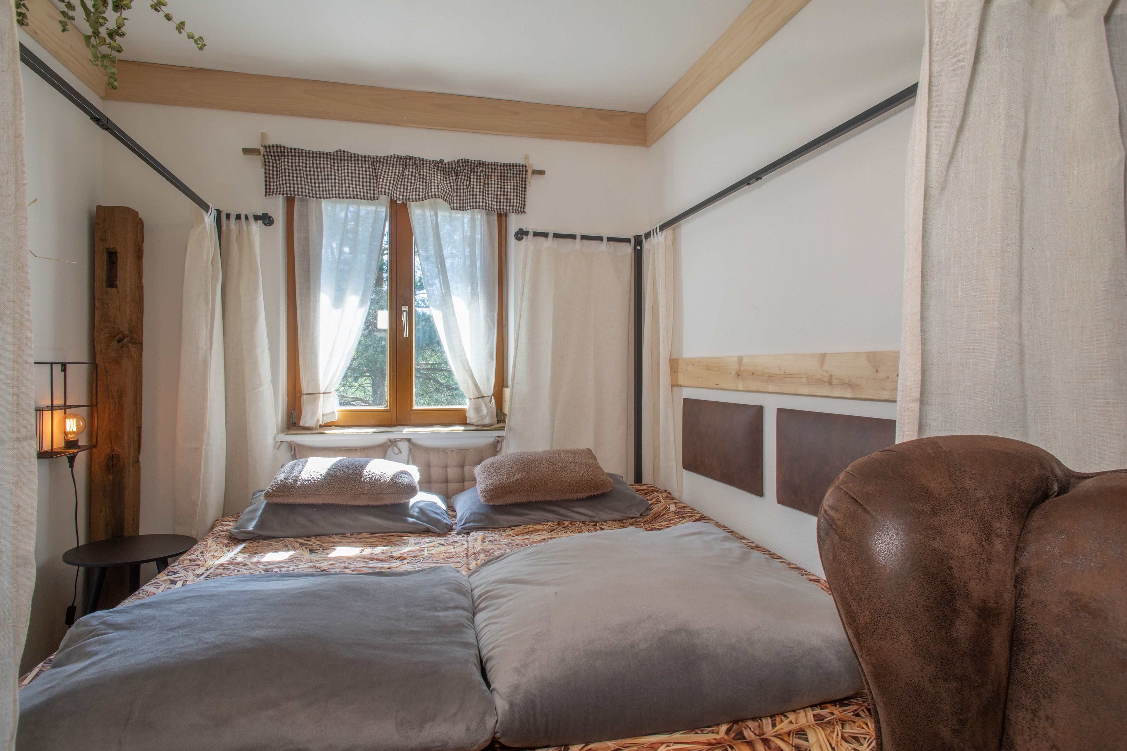 Ein Schlafzimmer mit einem großen Bett, einem Fenster mit Vorhängen, einem Holz-Kopfende und einem Nachttisch mit Lampe.