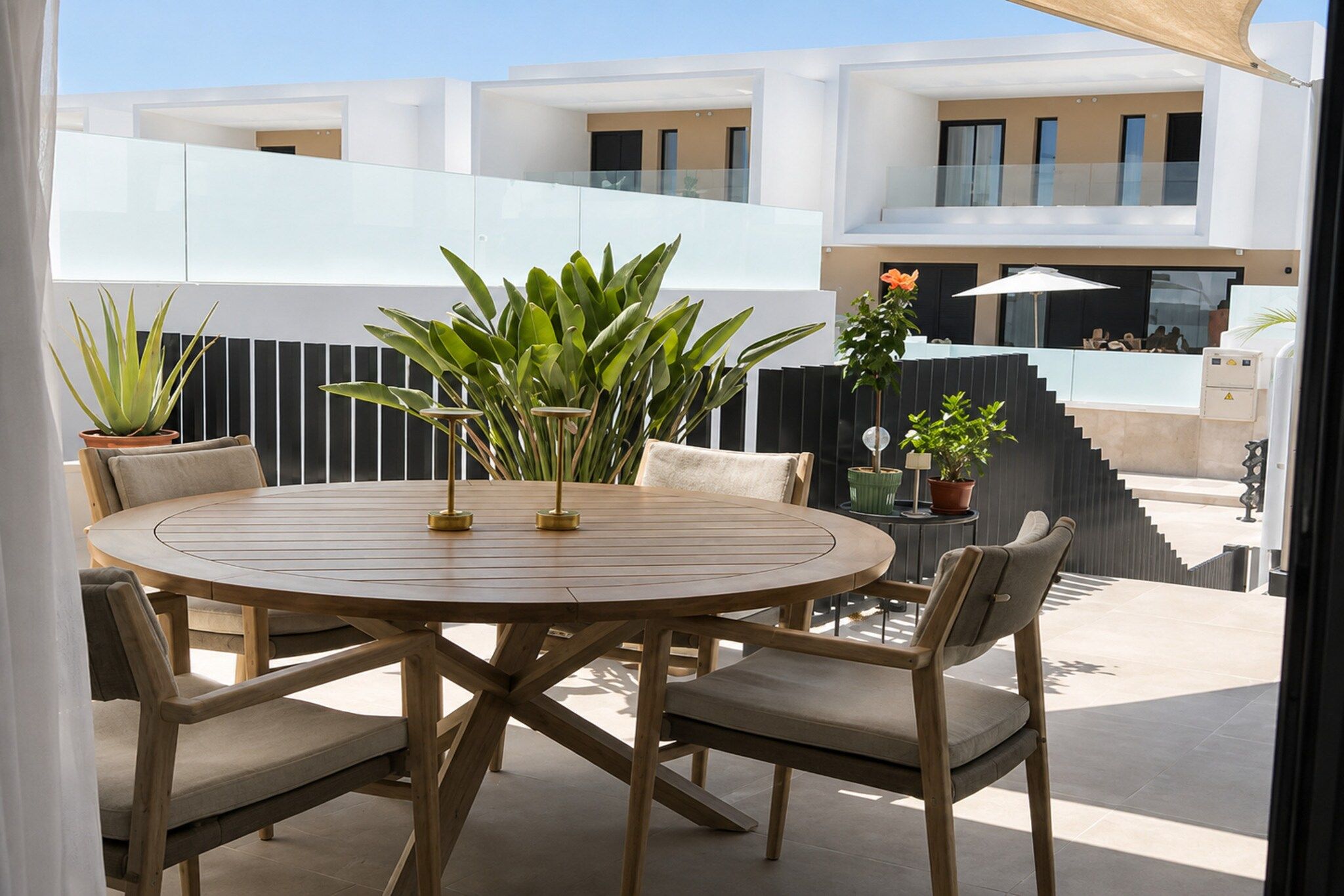 A round wooden table with chairs, surrounded by potted plants, in an outdoor patio area.