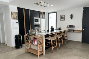 A modern kitchen with a central island, wooden chairs, and a black trash bin. - Casa del Sol – Exclusive Villa, Private Pool & Jacuzzi (Dolores)