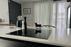 A modern kitchen with a black induction cooktop, a coffee maker, salt and pepper shakers, and a black cow-shaped decoration.