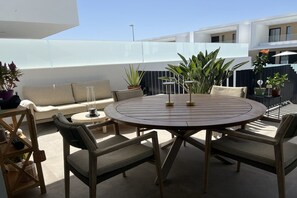 A round outdoor dining table with chairs, a sofa, and potted plants on a terrace.
