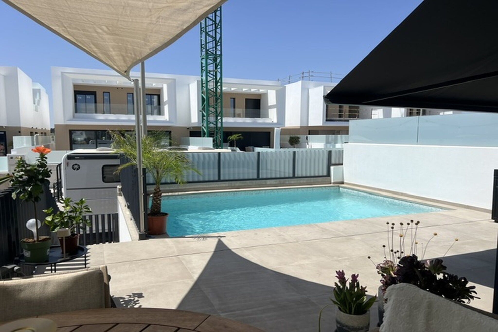 A rooftop pool area with a clear blue pool, potted plants, and a modern building in the background.