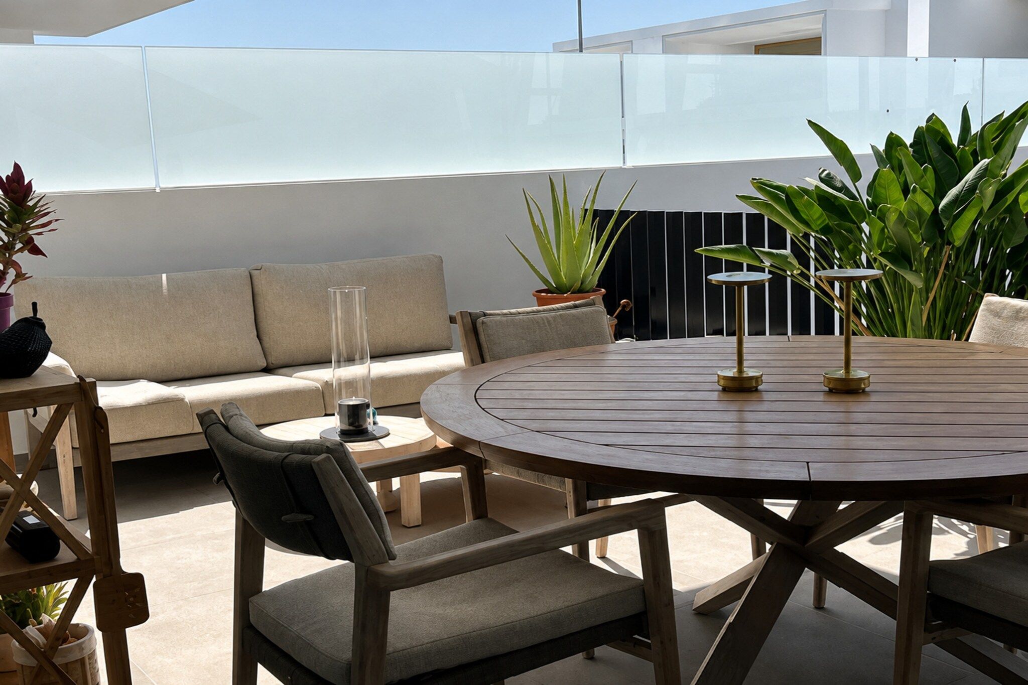 An outdoor patio with a round wooden table, cushioned chairs, a sofa, and potted plants.
