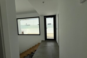 Ein schmaler Flur mit einer Holzbank, einem großen Fenster und einer Tür, die zu einem Außenbereich führt.