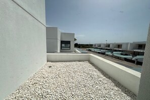 A rooftop terrace with a gravel floor, a modern building with a window, and a clear sky.