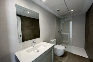 A modern bathroom with a large mirror, a white sink, a toilet, and a glass-enclosed shower area.