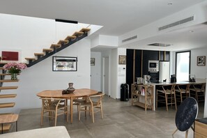 A modern kitchen with a central island, a dining area with a round table and chairs, and a staircase with wooden steps. - Casa del Sol – Exclusive Villa, Private Pool & Jacuzzi (Dolores)