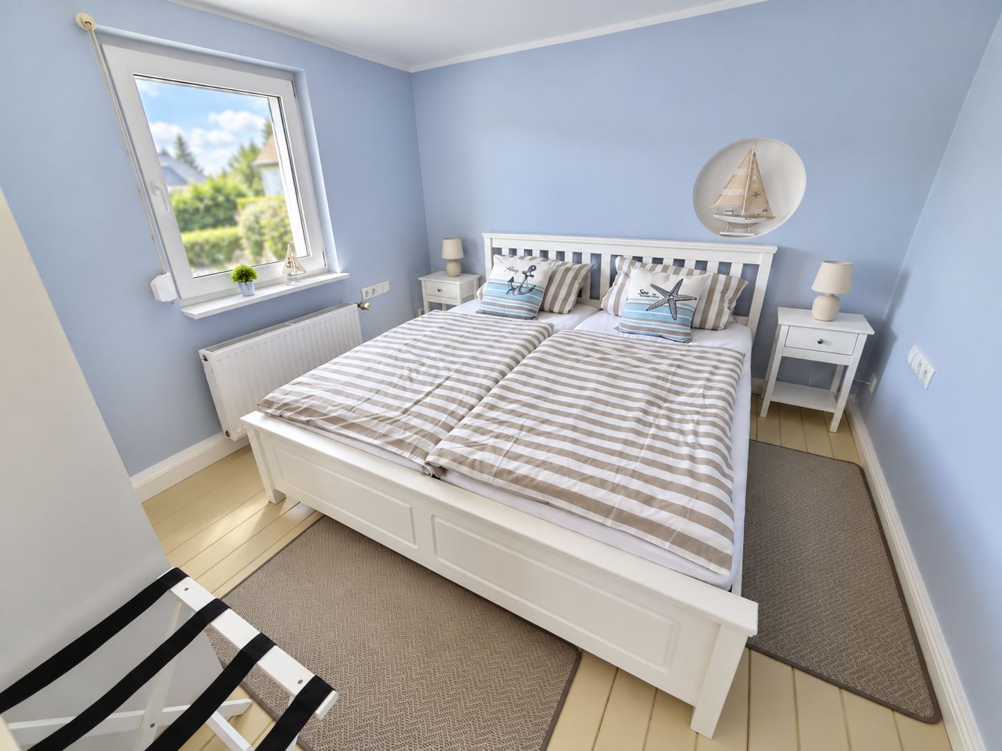 Une chambre à coucher avec un lit, deux tables de chevet, une fenêtre donnant sur un beau paysage et une décoration sur le thème de la voile.