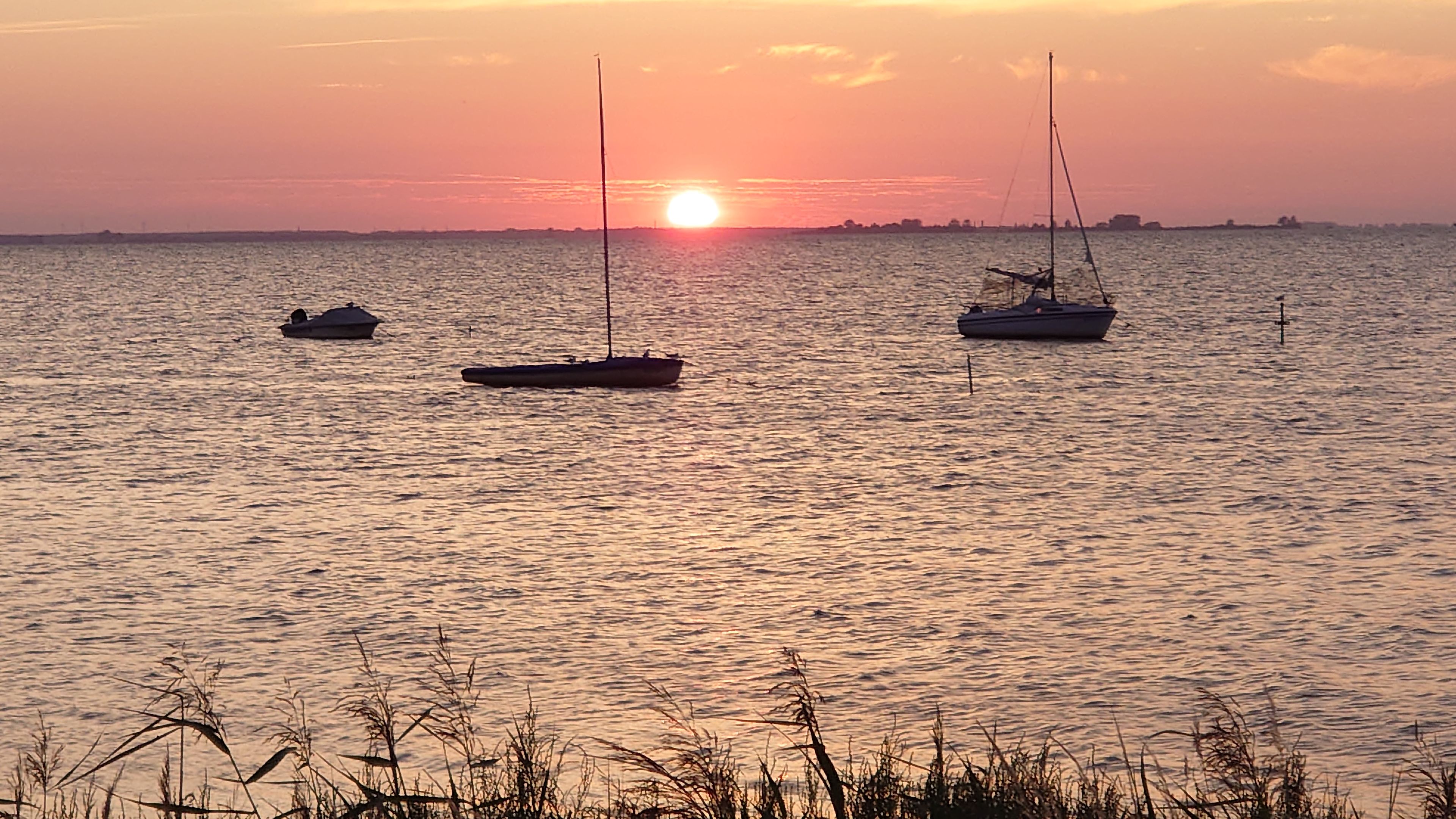Rustig water met drie boten bij zonsondergang.