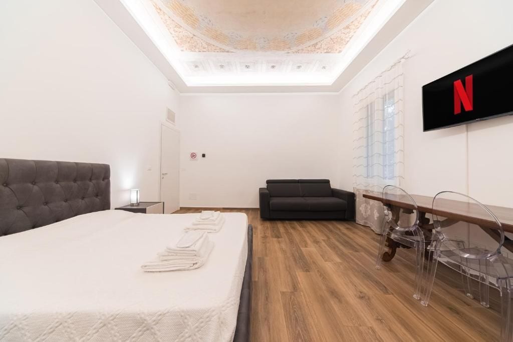 Ein Hotelzimmer mit einem Bett, einer Couch, einem an der Wand befestigten Fernseher und Holzboden.