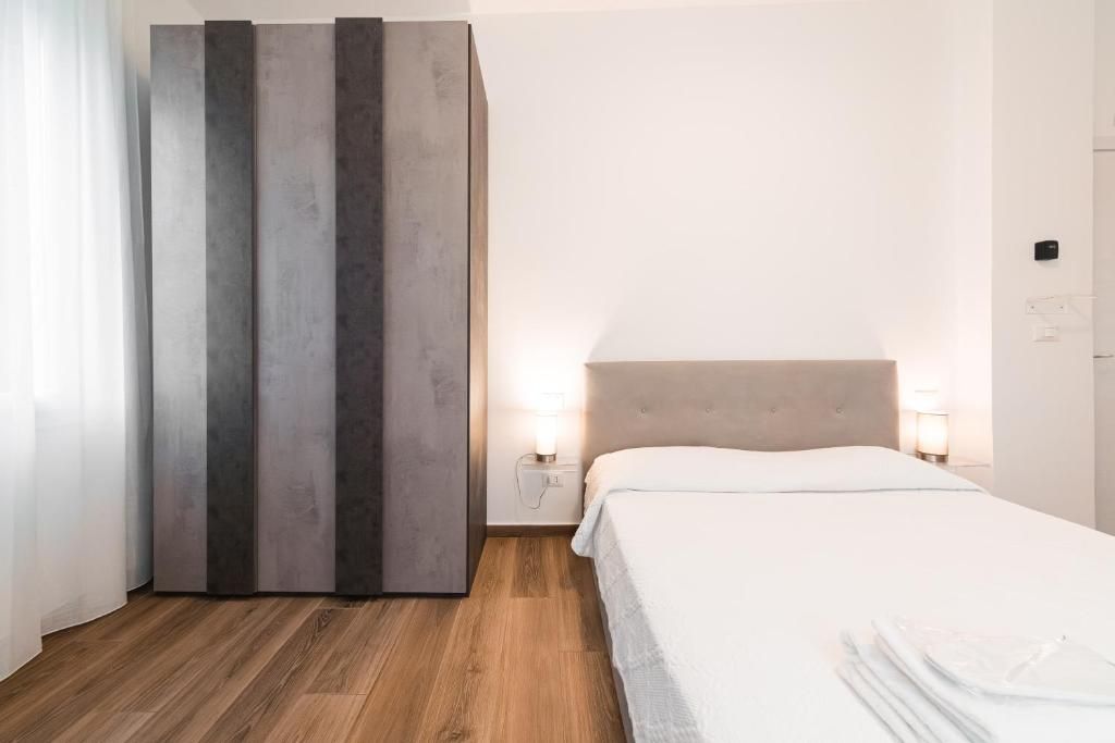 A hotel room with a bed, bedside lamps, a wardrobe, and a wooden floor.