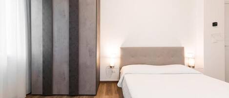 A hotel room with a bed, bedside lamps, a wardrobe, and a wooden floor.
