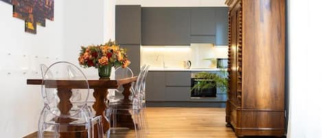 A modern kitchen with grey cabinets, a wooden dining table with clear chairs, and a large wooden cabinet.