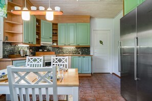 A kitchen with teal cabinets, a stainless steel refrigerator, and a dining area with white chairs. - Aurora Forest House, Sauna By Lapland Host (Rovaniemi)