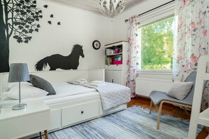 A bedroom with a bed, a chair, a radiator, a window with curtains, a wall clock, and a bookshelf. - Aurora Forest House, Sauna By Lapland Host (Rovaniemi)