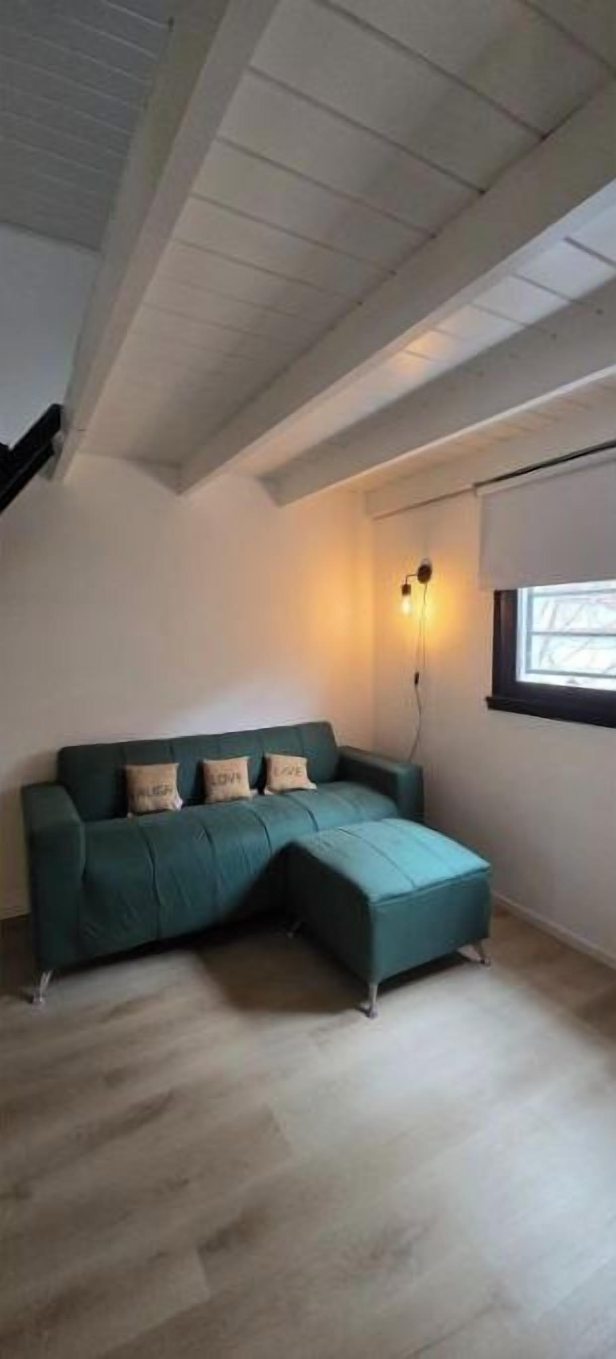 A room with a sectional sofa, a window with blinds, and a ceiling with exposed beams.