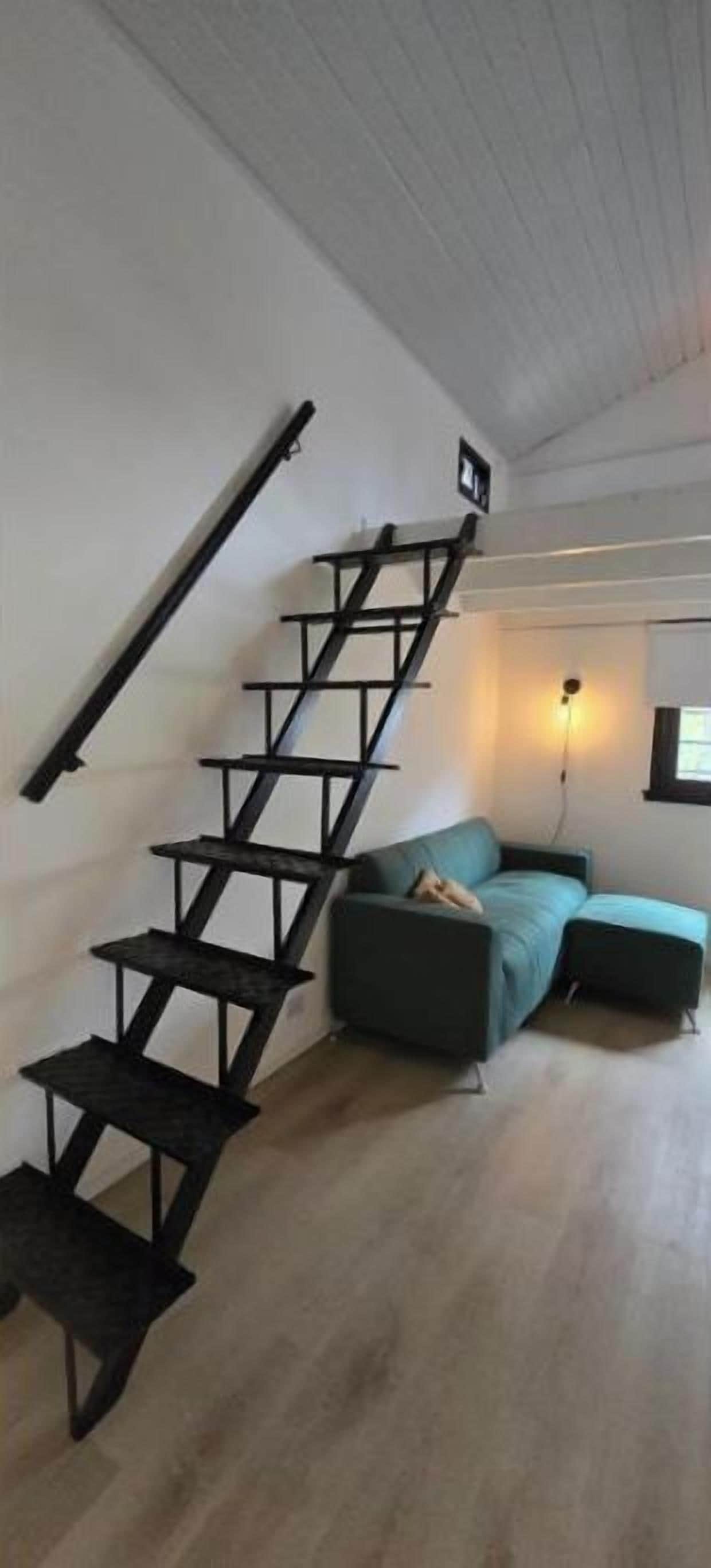 A staircase with a black metal railing leading to a landing. A green sofa is positioned in the room below the landing.