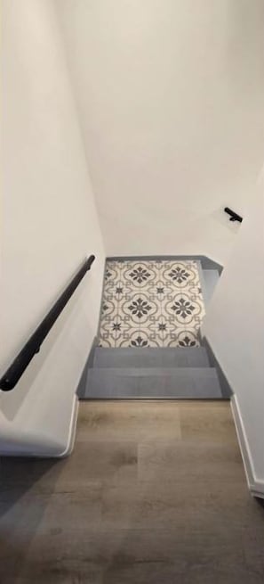 A narrow stairway with a handrail on the left and patterned floor tiles.