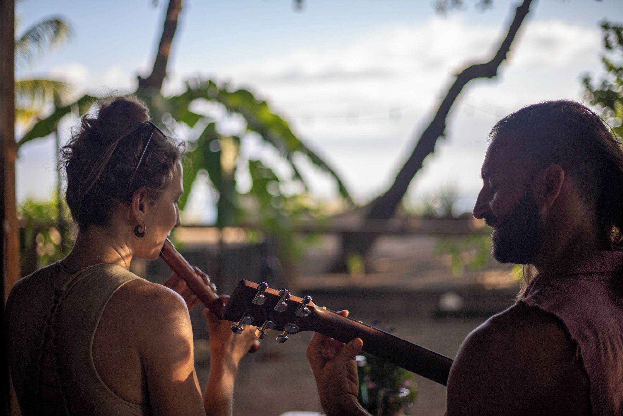 Deux personnes donnaient un concert en plein air, sous un ciel dégagé, avec des palmiers en arrière-plan.