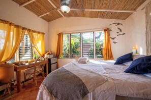 A room with a bed, a desk, and a chair. There is a window with curtains, a ceiling fan, and a wall with a light fixture. - Beachfront Cabina · Ocean & Sunset · Fiber WiFi&AC (nosara)