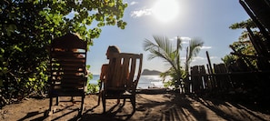 A beach scene with a wooden chair and a wooden structure, possibly a hut, with a view of the sea and palm trees.