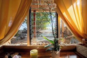 A room with a window, curtains, a potted plant, and a glass of water on a wooden table.