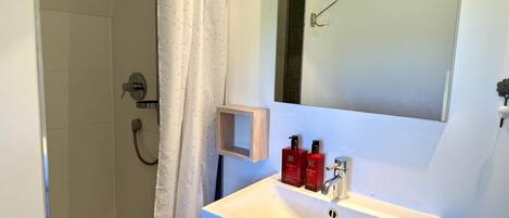 Un baño con lavamanos blanco, espejo y zona de ducha.