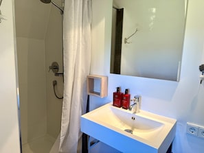 A bathroom with a white sink, a mirror, and a shower area. - Haus Westerheide - Vacation home for up to 4 people with a stunning view of the heath (List auf Sylt)
