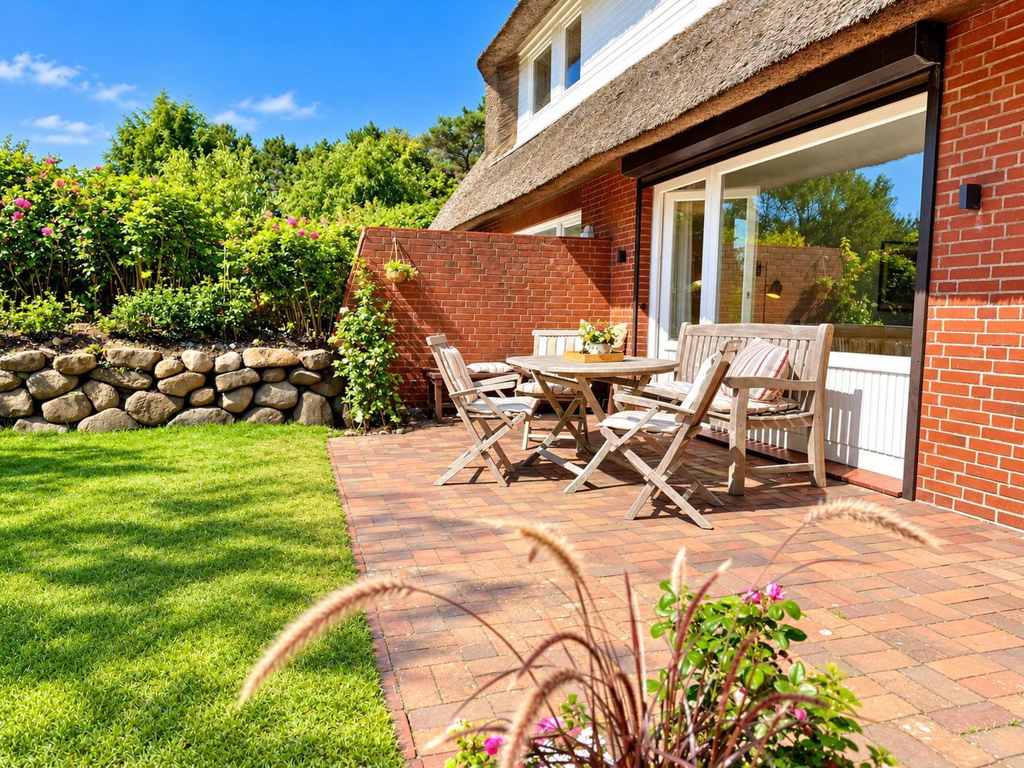 A patio with a table and chairs, a stone wall, and a grassy lawn.