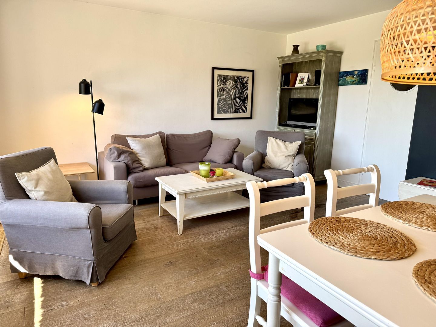Ein Wohnzimmer mit einer Couch, Sesseln, einem Couchtisch und einem Esstisch mit Platzdeckchen.