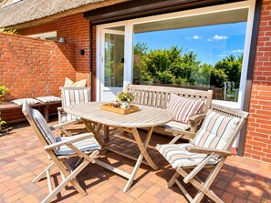 An outdoor patio with a round wooden table, four striped lounge chairs, and a brick wall. - Haus Westerheide - Vacation home for up to 4 people with a stunning view of the heath (List auf Sylt)