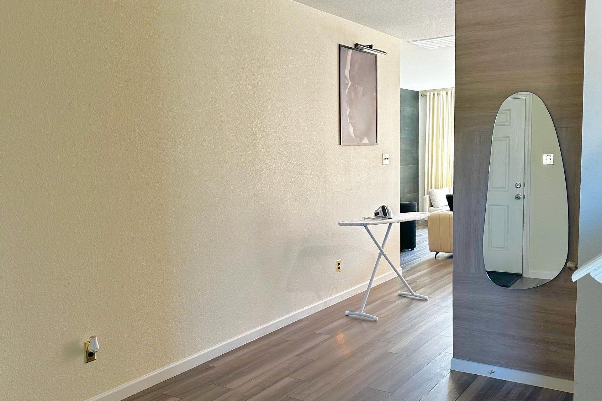 A hallway with a wooden floor, a white door, and a small table with an ironing board.