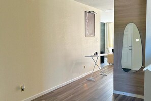 A hallway with a wooden floor, a white door, and a small table with an ironing board. - Luxury 5BR Designer Home • Sleeps 15 • Near Dallas • Extended & Short Stays (Glenn Heights)