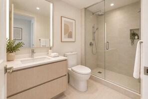 Ein modernes Badezimmer mit einer Duschkabine, einer weißen Toilette und einem Waschbecken mit Spiegel.