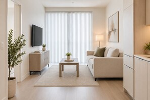 Ein modernes Wohnzimmer mit einer Couch, einem Couchtisch, einem Fernseher und einem großen Fenster mit Jalousien.