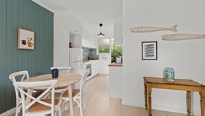 Eine moderne Küche mit weißen Schränken, einem Holztisch und Stühlen. An den Wänden befinden sich Bilder von Fischen, und ein kleiner Tisch steht mit einer Vase darauf.