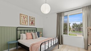 Ein Schlafzimmer mit Bett, Nachttisch, einem Fenster mit Vorhängen und Wandbildern.