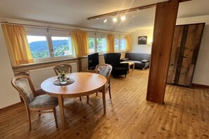 A room with a round wooden table, four chairs, a sofa, and a window with curtains. - Holiday apartment in Todtnau with barbecue (Todtnau)