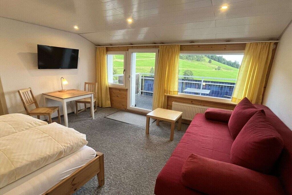 Ein Hotelzimmer mit einem Bett, einem roten Sofa, einem Schreibtisch mit Stuhl, einem an der Wand befestigten Fernseher und einem Fenster mit Vorhängen.